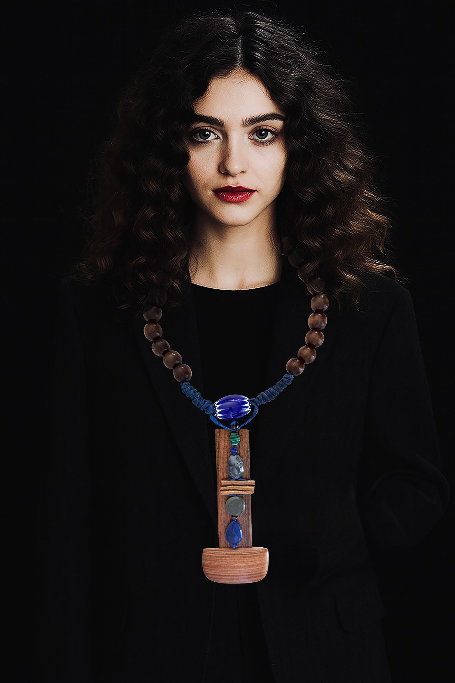  A quiet sculptural presence. One-of-a-kind sculptural necklace built around an  architectural bookmark wooden pendant — vertical, solid, grounded. Various stones, golden coral, a Venetian (Murano)chevron trade glass bead, wood beads on Cobalt blue adjustable braided threads complete this unique piece handmade in Lebanon with materials sourced all over the world. 
An Architectural and tactile totem. 