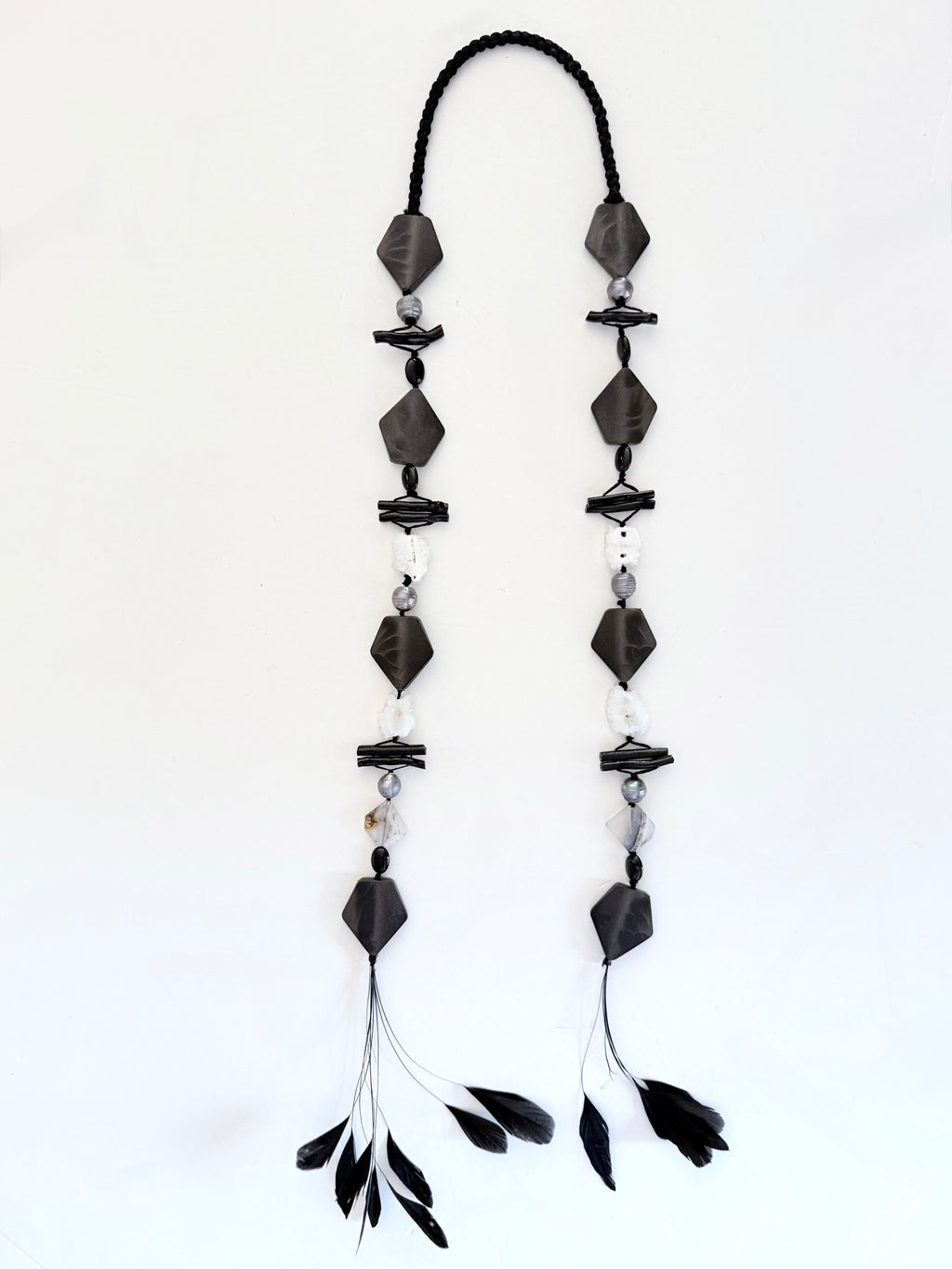 Ritualistic. Tribal Modern aesthetic. Unique piece long open drop necklace, handmadein Lebanon with materials sourced worldwide.Black geometric shapes, pearls,onyx,black coral, druzy quartz and feather tassels.Raw materials. Double feather pendants. Sophisticated, collectible, wearable artifact.